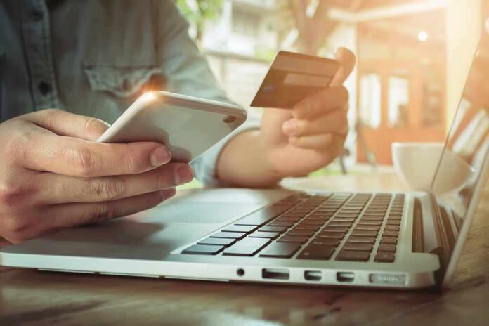 Hands using smartphone and credit card beside a laptop