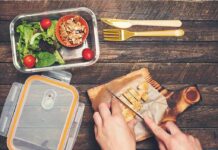 Hands slicing cooked chicken on a wooden cutting board