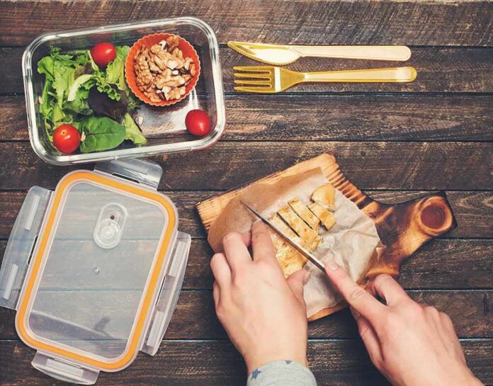 Hands slicing cooked chicken on a wooden cutting board