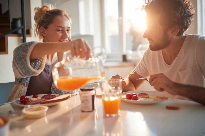1783888970694-aujihm-shutterstock-1900442887 Couple eating breakfast with orange juice at a sunlit table