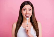 Woman holding a fork to her teeth against a pink background