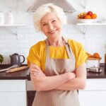 Smiling older woman in apron standing in a bright kitchen