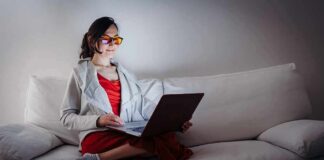 Person wearing orange glasses using a laptop on a white couch