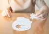 Person holding puzzle piece over head-shaped jigsaw on table