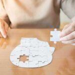 Person holding puzzle piece over head-shaped jigsaw on table