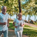 Two adults jogging on a tree-lined lakeside path