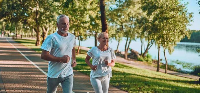 Two adults jogging on a tree-lined lakeside path