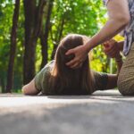 Person assisting someone lying on a path in a park