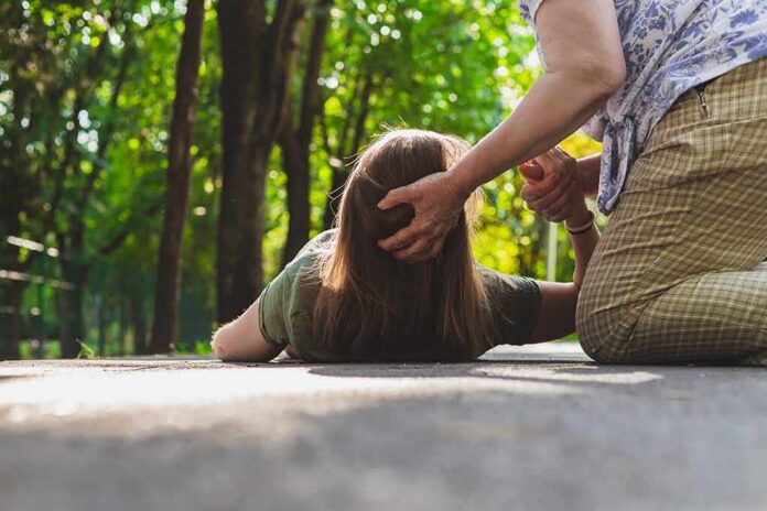 Person assisting someone lying on a path in a park