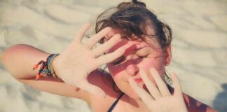 woman on beach shielding eyes with sandy hands