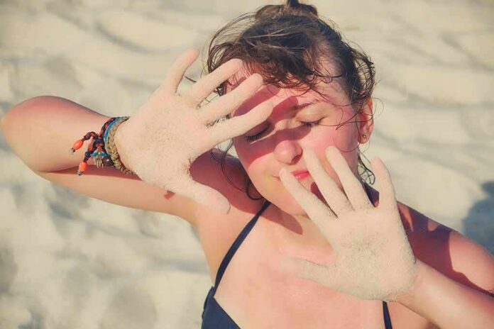 woman on beach shielding eyes with sandy hands