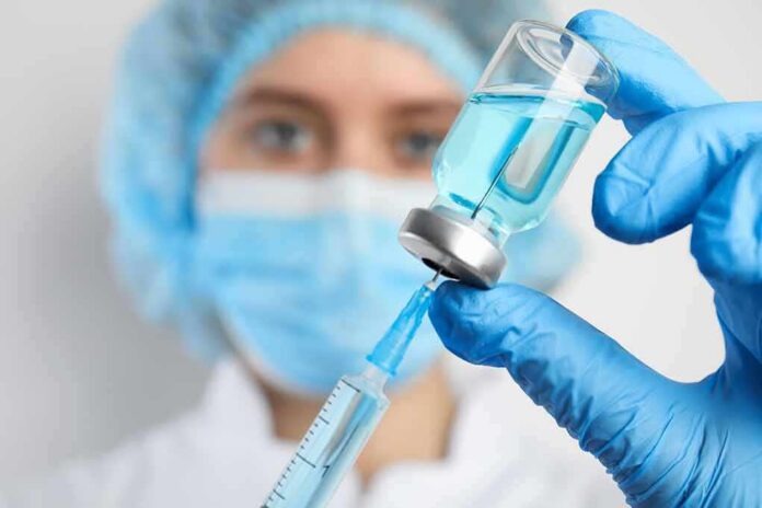 Healthcare worker drawing blue liquid from vial with syringe