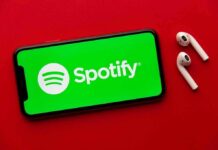 Smartphone with Spotify app and wireless earbuds on red background