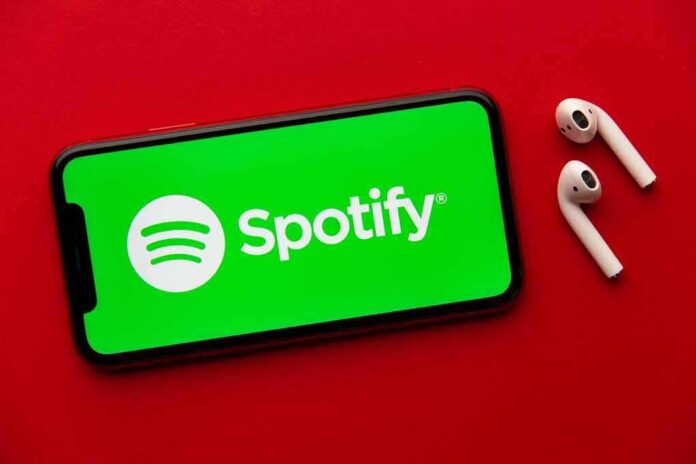 Smartphone with Spotify app and wireless earbuds on red background