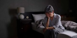 Older adult sitting on bed with head in hand