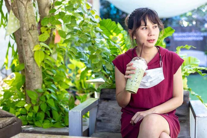 Woman in red dress drinking iced matcha in a garden
