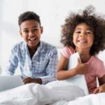two smiling children sitting on a bed