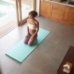 woman kneeling on yoga mat in bright kitchen near pool