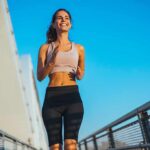 Smiling woman jogging on a bridge under a clear blue sky