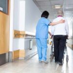 Nurse assisting an elderly person with a walker in a hallway