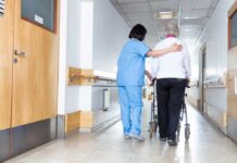 Nurse assisting an elderly person with a walker in a hallway
